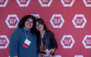 Two woman smiling in front of a red backdrop.